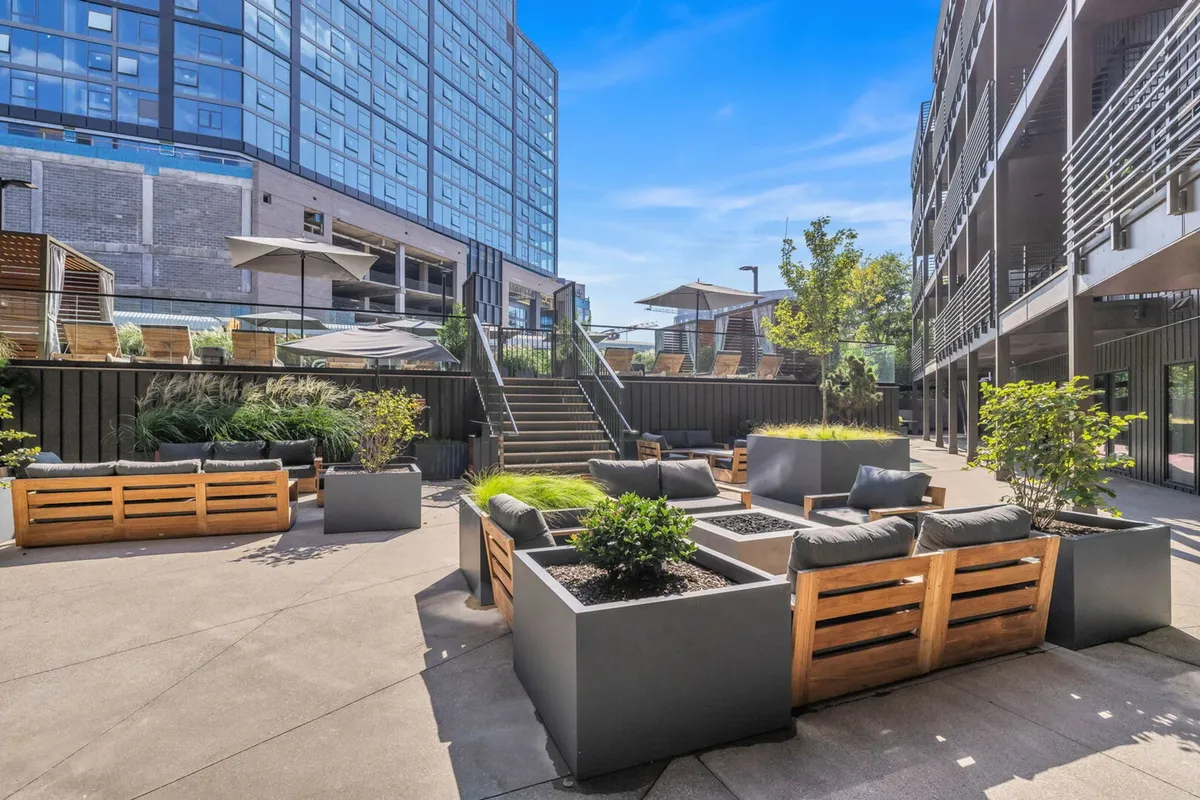 A vibrant rooftop lounge space featuring modern outdoor seating, lush greenery, and a staircase leading to an upper level. The arrangement encourages social gatherings and offers open-air views, perfect for group celebrations and enjoying the city atmosphere.