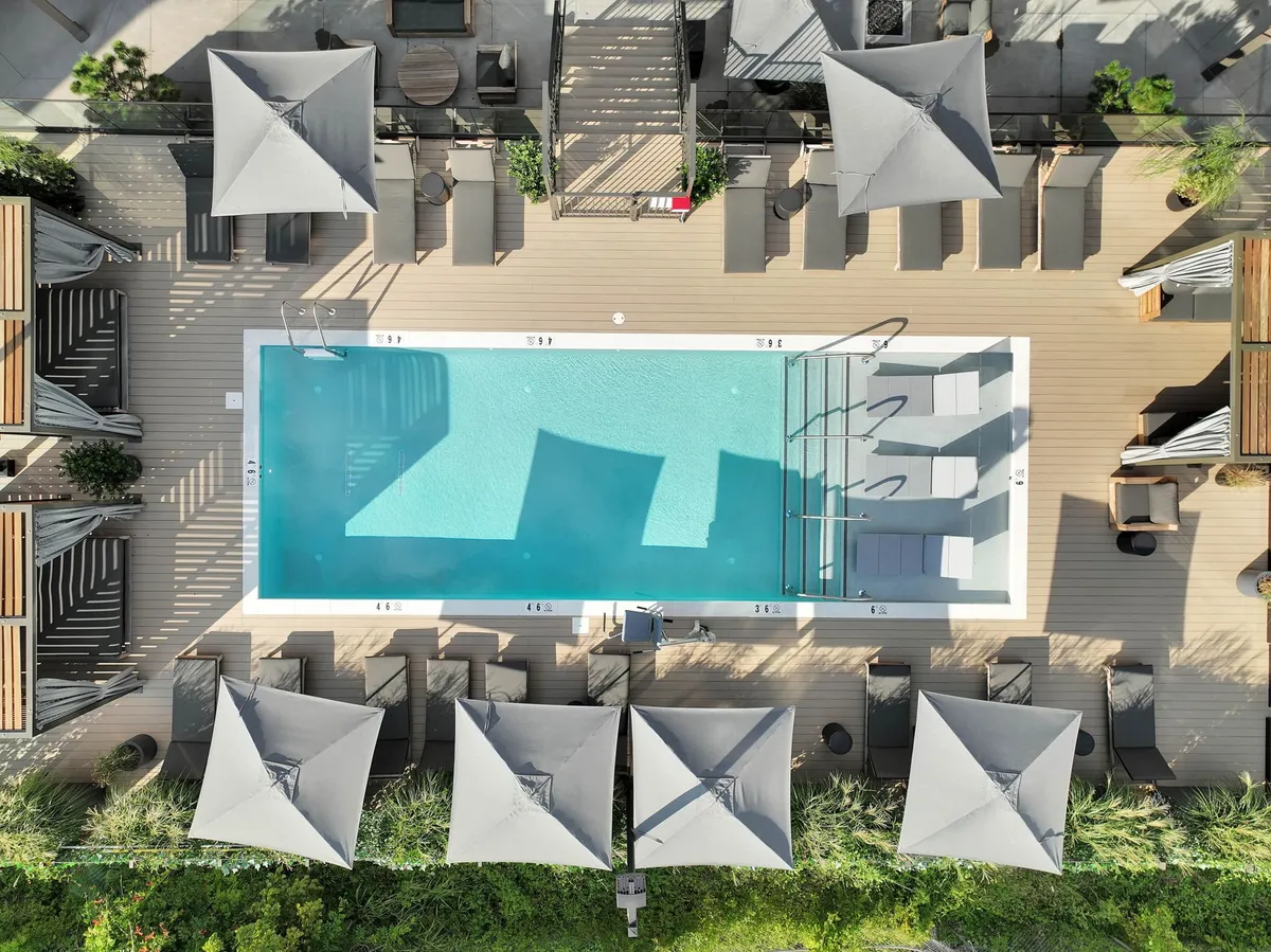 A tranquil swimming pool area featuring sun loungers, shade umbrellas, and a spacious deck. The setting encourages relaxation, with clear water reflecting the sky and plenty of seating options for sunbathing or socializing. The overall mood is calm, inviting, and refined, perfect for enjoying warm-weather swims or poolside gatherings.