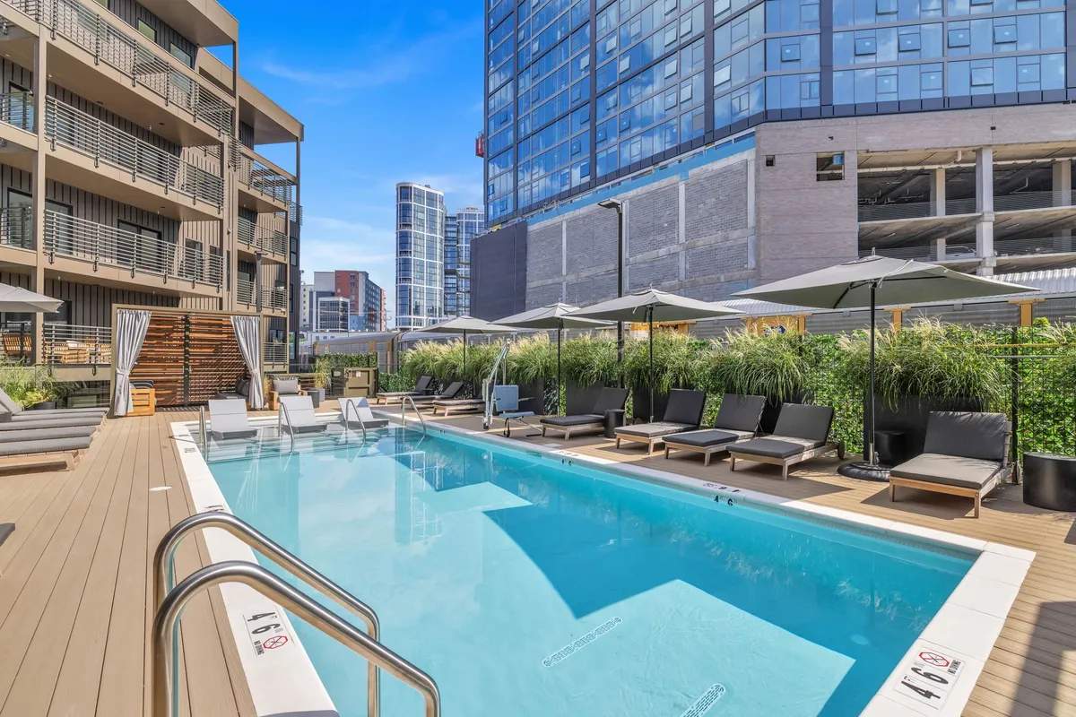 A stylish exterior pool area with lounge chairs, umbrellas, and the building's modern facade in view. This communal outdoor amenity is designed for sunbathing, swimming, and social events, fostering a sense of shared enjoyment.