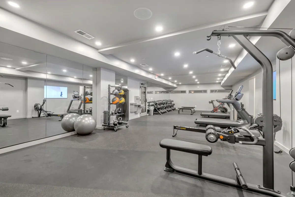 A bright, modern fitness center filled with a variety of exercise machines, including treadmills and a weights rack. The space is well-lit and energetic, designed to inspire workouts and support fitness goals. Large mirrors and organized equipment give the facility a contemporary and motivating feel.