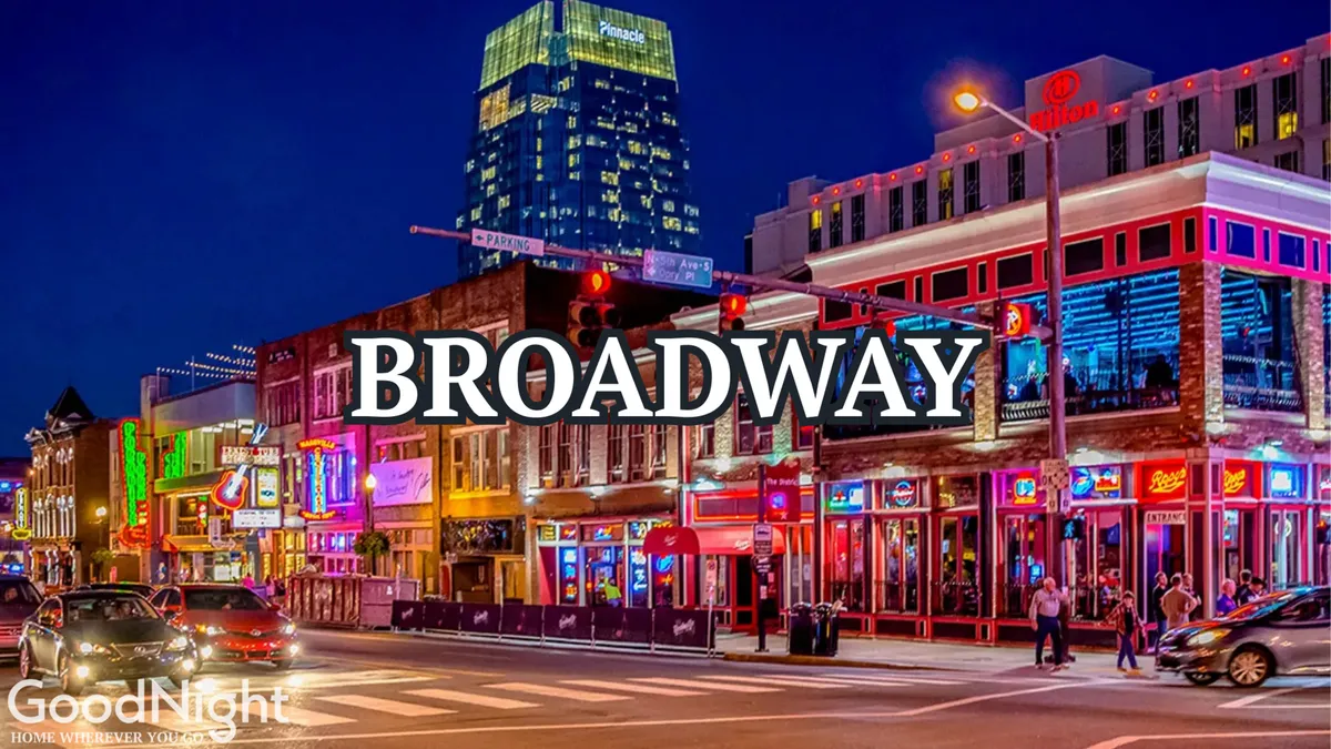 A vibrant street scene on Broadway in Nashville, filled with neon signs, bustling crowds, cars, and brilliantly illuminated buildings. The energy of live performances and nightlife spills onto the sidewalk, perfectly capturing the city's legendary honky-tonk atmosphere.