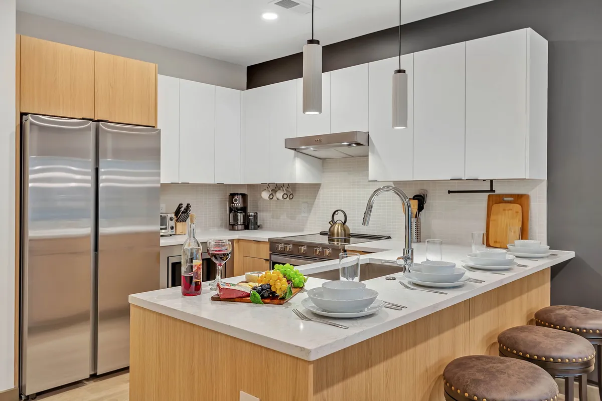 The kitchen is the focal point here, featuring a generous island, elegant dining table settings, stainless steel appliances, and fresh produce displayed on the counter. The setting exudes warmth and readiness for hosting meals or casual gatherings.