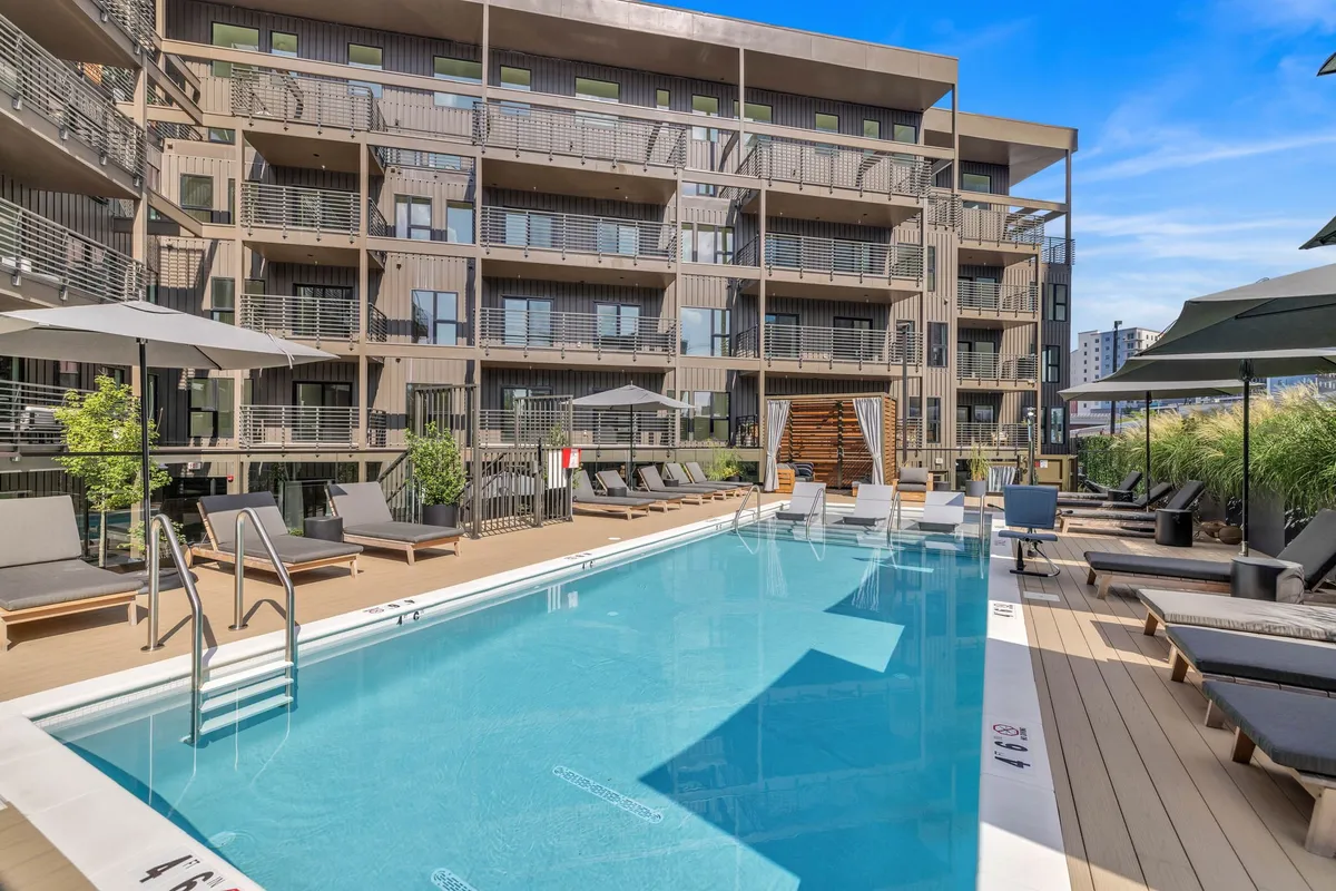 The exterior pool area features a sparkling swimming pool, lounge chairs, umbrella shades, and the apartment building facade. The space looks inviting and perfect for family leisure during the warmer months.