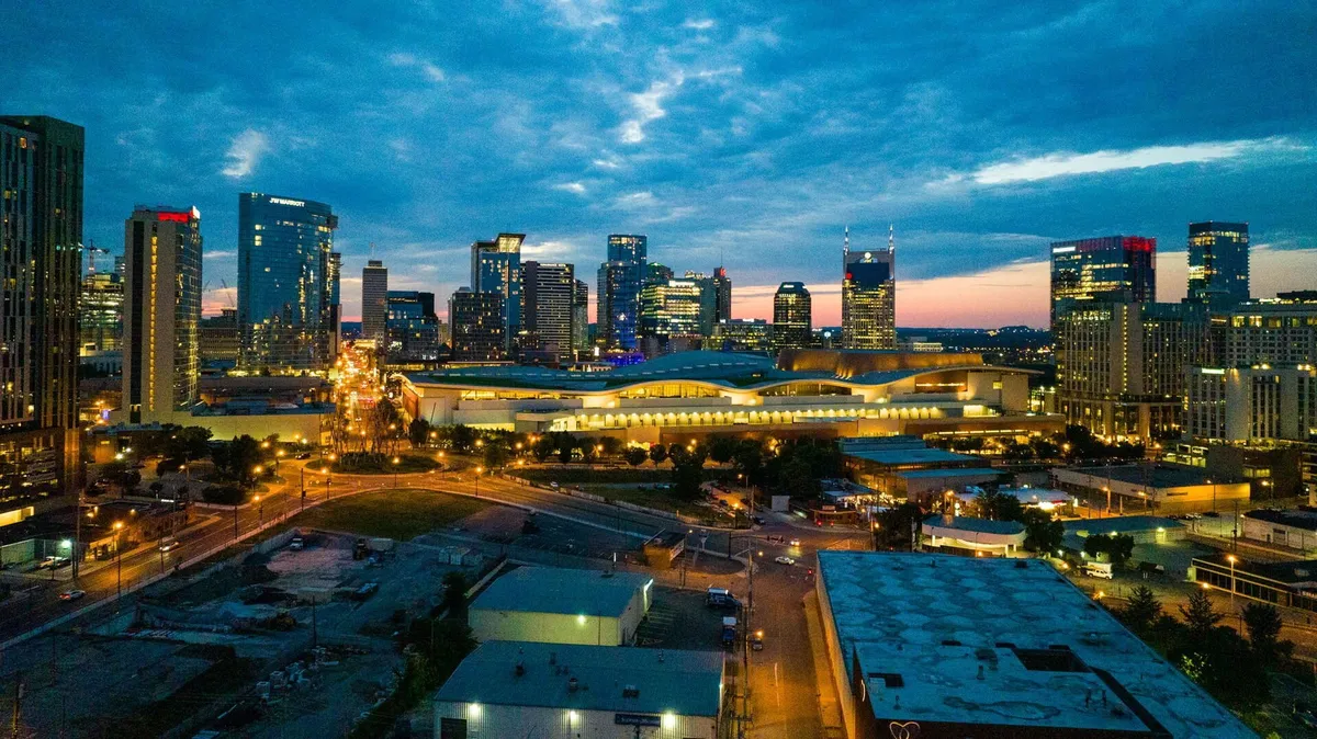 A rooftop lounge with panoramic views of the city skyline at dusk. The illuminated buildings and vibrant dusk sky create an energetic, celebratory mood, suggesting a perfect spot for special occasions or sunset selfies.