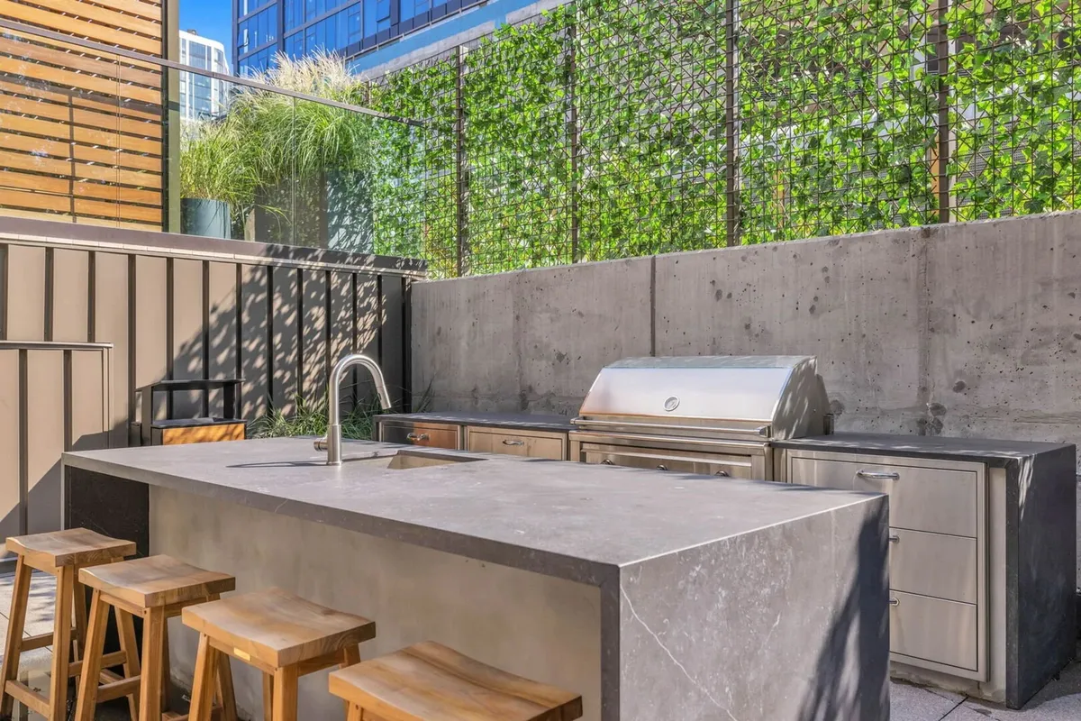A contemporary outdoor kitchen island with a grill, bar stools, and a lush greenery wall. The setup is ideal for outdoor cooking, casual dining, and group gatherings, evoking a sense of community and upscale leisure.