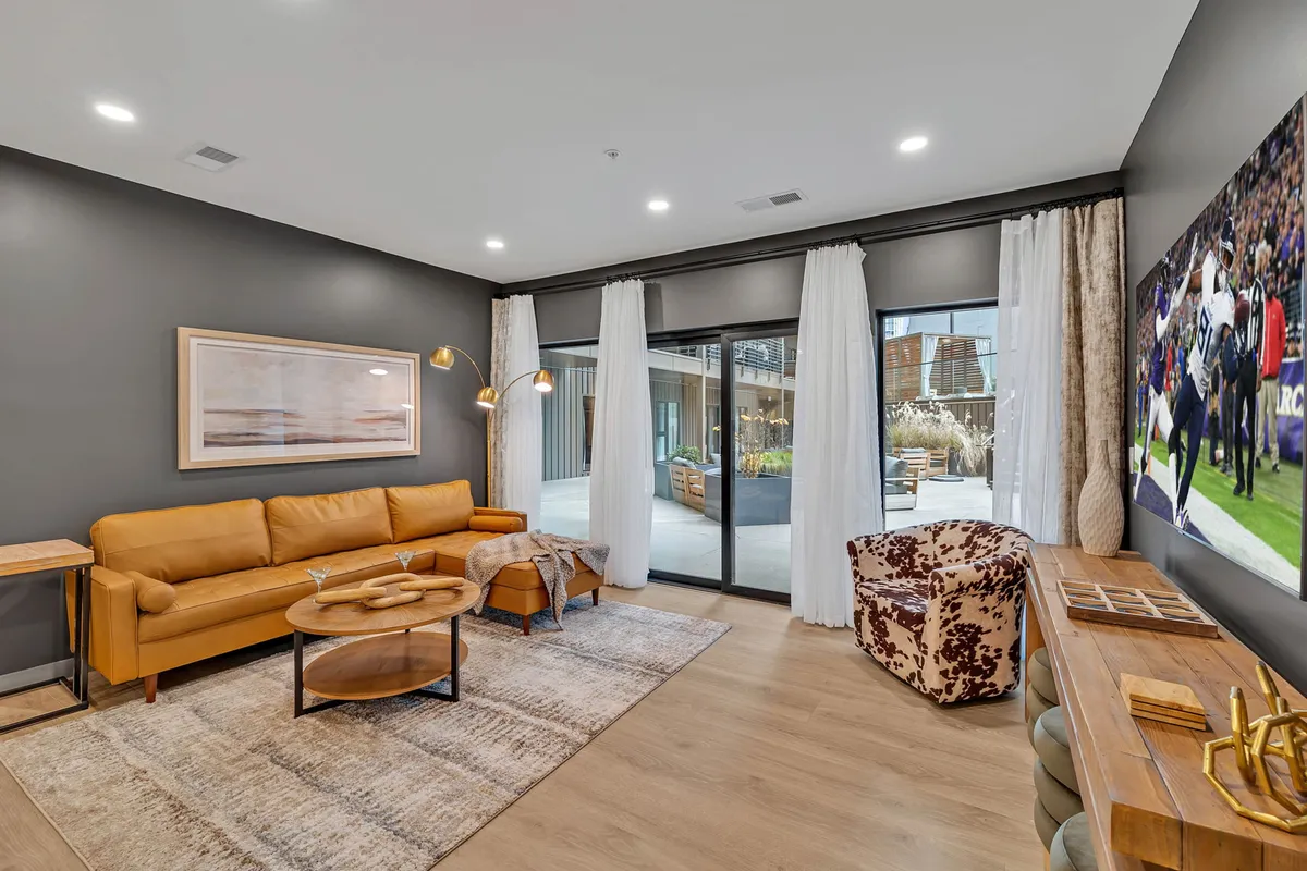 A comfortable interior shot with a yellow leather sofa, a large wall-mounted TV, a wooden coffee table, and lively room accents. The space invites guests to relax, watch TV, or socialize in a cheerful environment.
