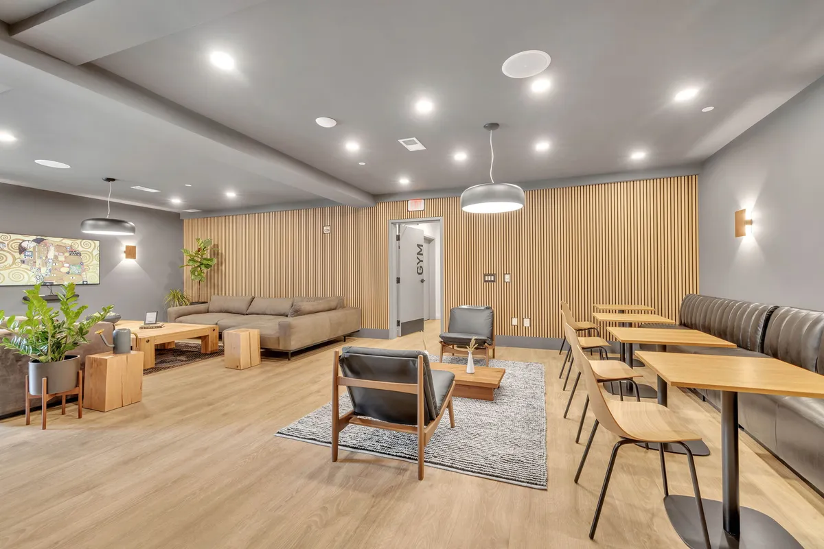 A spacious, modern lobby area featuring modular seating, wooden wall paneling, contemporary artwork, potted plants, and inviting light fixtures. The layout suggests a welcoming entry experience and a space designed for both gathering and relaxation.